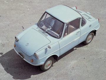 Vintage Mazda R360 compacte auto met een opvallende belvorm, geparkeerd op een betonnen ondergrond.