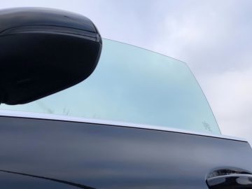 Zijaanzicht van een Mercedes-Benz CLA met een zijspiegel, raam en een deel van het dak tegen een bewolkte hemel.