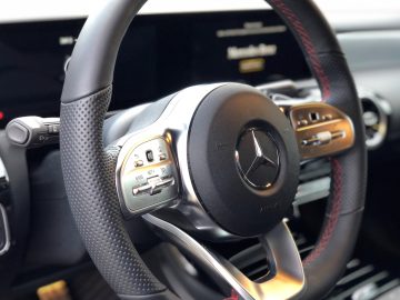 Binnenaanzicht van het stuur van een moderne Mercedes-Benz CLA met bedieningselementen, voorzien van een Mercedes-Benz-logo.