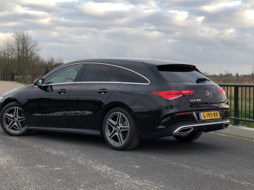 Zwarte Mercedes-Benz CLA geparkeerd op een verhard terrein met een bewolkte lucht op de achtergrond.