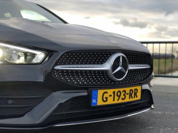 Close-up van een zwarte Mercedes-Benz CLA-autogrille en badge met koplampen aan.