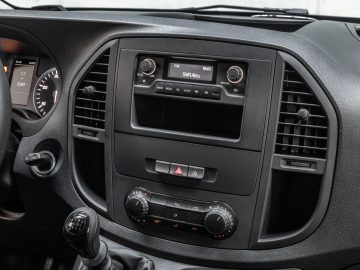 Binnenaanzicht van het dashboard van de Mercedes-Benz Vito, met de nadruk op de middenconsole, die een radiodisplay, een alarmlichtknop en knoppen voor de klimaatregeling omvat.