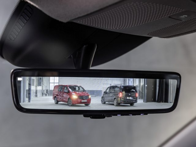Achteruitkijkspiegelperspectief van een Mercedes-Benz Vito en een ander voertuig geparkeerd in een gebouw.