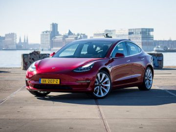 Rode Tesla model 3, Auto van het Jaar 2020, geparkeerd aan de waterkant op een heldere dag.
