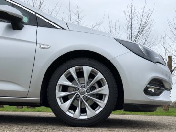 Zilverkleurige Opel Astra Sports Tourer geparkeerd op de stoep, met de nadruk op het voorwiel en het spatbord.