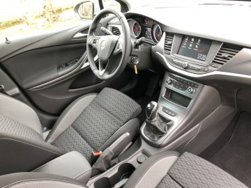 Binnenaanzicht van een Opel Astra Sports Tourer met stoffen stoelen, een stuur met gemonteerde bedieningselementen, een middenconsole met entertainmentsysteem en een automatische versnellingspook.