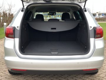 Een open kofferbak van een zilverkleurige Opel Astra Sports Tourer met een ruime en lege laadruimte.
