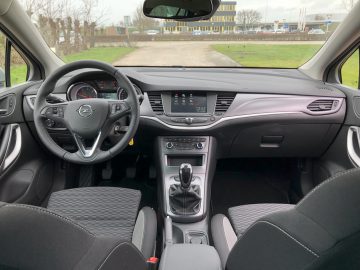Binnenaanzicht van een Opel Astra Sports Tourer met stuur en dashboard zichtbaar, geparkeerd met zicht op buiten door de voorruit.