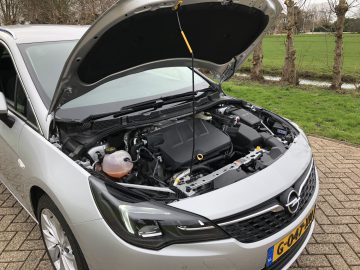 Een zilverkleurige Opel Astra Sports Tourer met de motorkap open en de motorruimte zichtbaar.