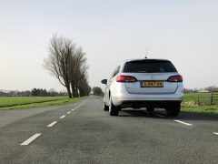 Een Opel Astra Sports Tourer die op een heldere dag wegrijdt op een landelijke weg met bomen en een open veld.