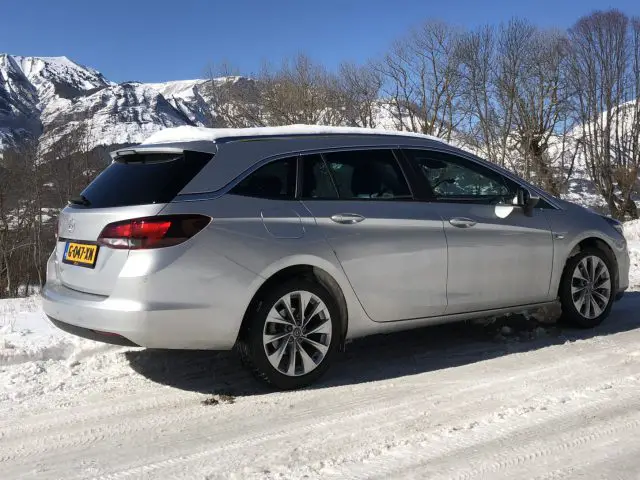 Zilveren Opel Astra Sports Tourer stationwagen op een besneeuwde weg met bergen op de achtergrond.