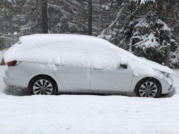 Een Opel Astra Sports Tourer bedekt met een dikke laag sneeuw, geparkeerd voor een besneeuwd bos.