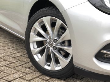 Close-up van de lichtmetalen velgen en band van een Opel Astra Sports Tourer, geparkeerd op een bakstenen oppervlak.