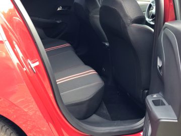 De open deur van de rode Opel Corsa toont het interieur met zwarte stoelen en rode stiksels.