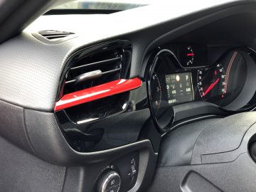 Binnenaanzicht van een Opel Corsa met een digitaal dashboard en een open dashboardkastje.
