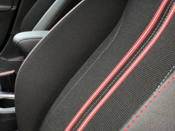 Close-up van een Opel Corsa-autostoeltje met zwarte bekleding en rode stiksels.
