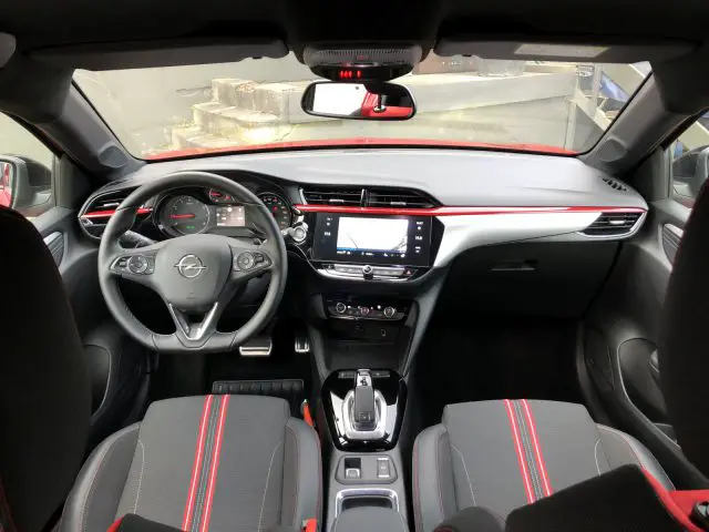 Interieur van een moderne Opel Corsa met een zwart-rood kleurenschema met het dashboard, het stuur en het infotainmentsysteem.