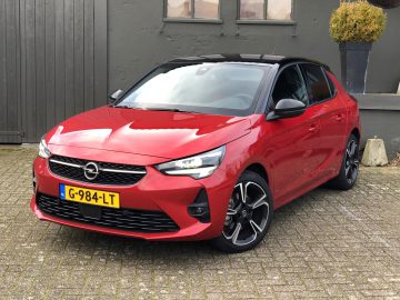 Rode Opel Corsa geparkeerd voor een gebouw met grijze muren.