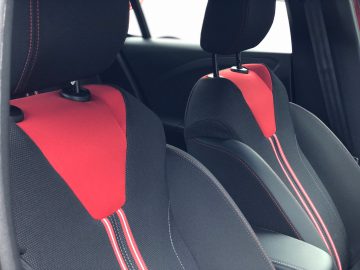 Binnenaanzicht van de voorstoelen van een Opel Corsa met rode en zwarte bekleding.