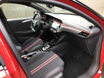 Opel Corsa-interieur met rode en zwarte bekleding, met een stuur, digitaal dashboard en centraal touchscreen.