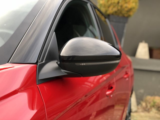 Rode Opel Corsa met een close-up van de zijspiegel.