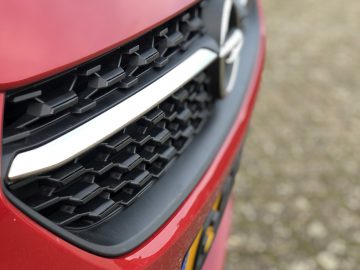 Close-up van de grille van een rode Opel Corsa met de focus op het grillepatroon en het embleem.