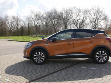Oranje Renault Captur compacte Suv geparkeerd op een zonnige dag met bomen op de achtergrond.