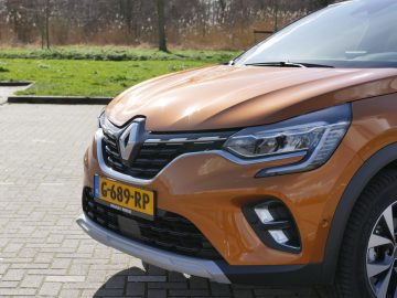 Close-up van een oranje Renault Captur die buiten geparkeerd staat, met het voorste gedeelte en het logo van de fabrikant.