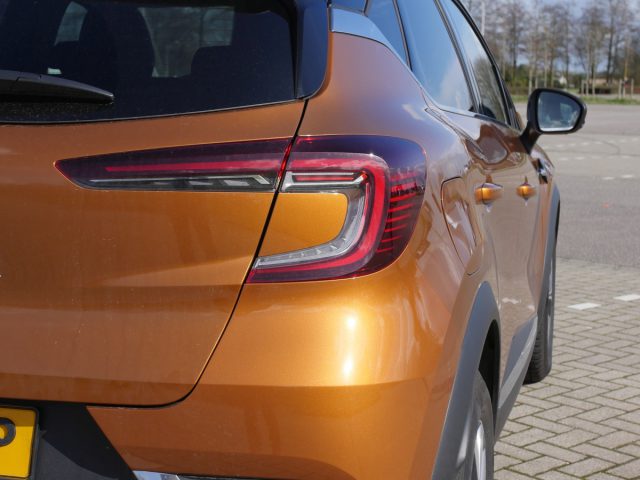 Close-up van het achterste zijgedeelte van een oranje Renault Captur met zichtbaar achterlicht en kentekenplaat.