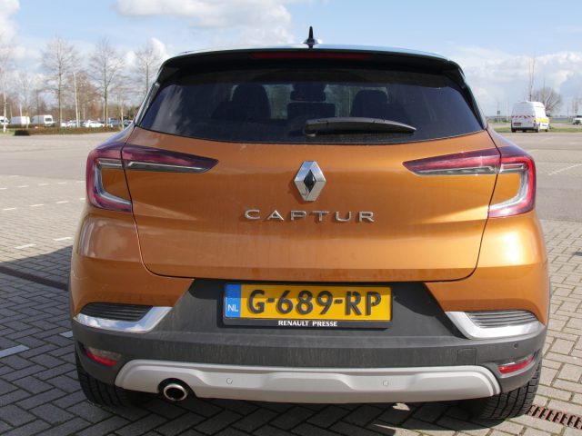 Achteraanzicht van een oranje Renault Captur geparkeerd op een buitenterrein met Nederlandse kentekenplaten.