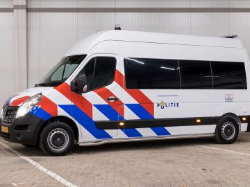 Nederlands politievoertuig, een Renault Master met opvallende kleurstelling, geparkeerd in een garage.