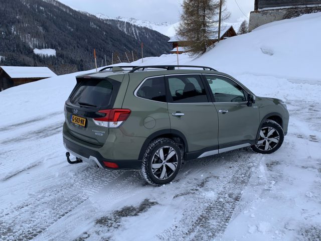 Een groene Subaru Forester e-boxer geparkeerd op een besneeuwde weg met bergachtig terrein op de achtergrond.