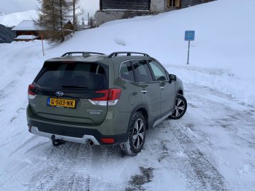 Een groene Subaru Forester e-boxer geparkeerd op een besneeuwde weg in een bergachtig gebied.