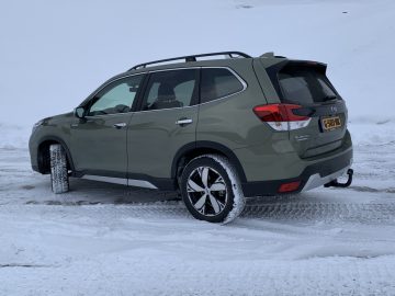 Groene Subaru Forester e-boxer geparkeerd op een met sneeuw bedekt terrein.