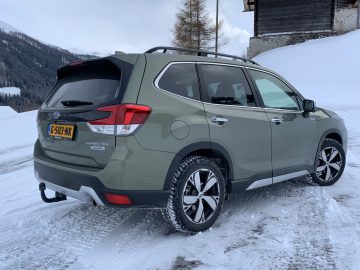 Een groene Subaru Forester e-boxer geparkeerd op een besneeuwde weg met bergen op de achtergrond.
