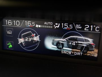 Het digitale display van een Subaru Forester e-boxer met de instellingen voor de klimaatregeling, de tijd, de buitentemperatuur en een afbeelding van de auto op besneeuwd terrein met ingeschakelde tractiemodus.