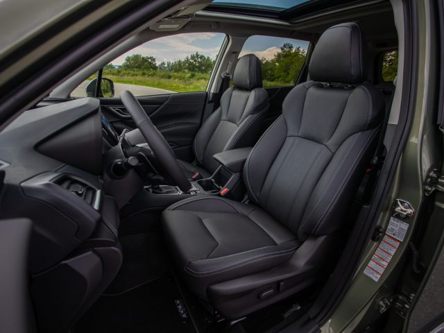 Zijaanzicht van het interieur van een Subaru Forester e-boxer met zwartleren stoelen, een stuur en een dashboard met infotainmentsysteem.