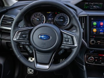Een close-up van het stuur en het dashboard van een Subaru Forester e-boxer, met bedieningselementen en digitale schermen.