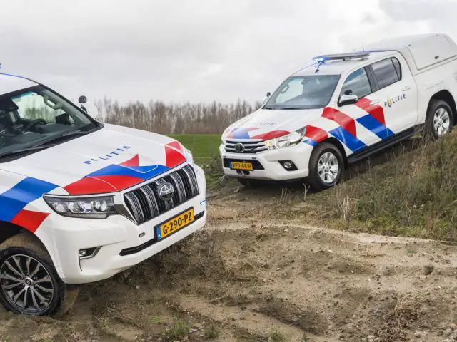 Twee Toyota-politievoertuigen geparkeerd op oneffen terrein met noodverlichting aan.