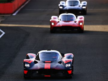 Drie krachtige Aston Martin-sportwagens die achter elkaar op een racecircuit rijden.