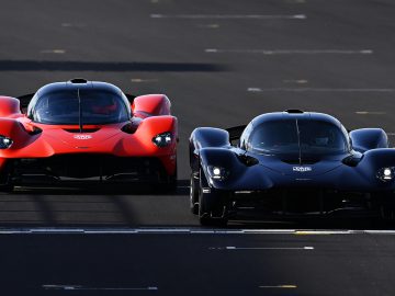 Twee krachtige Aston Martin-voertuigen, een rode en een blauwe, staan naast elkaar op een circuit en laten hun aerodynamische ontwerpen zien.