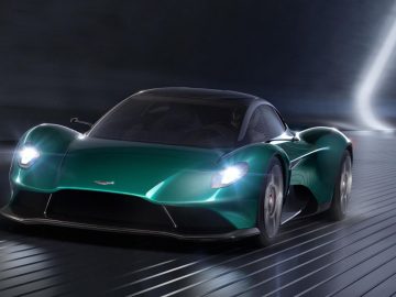 Een strakke groene Aston Martin-sportwagen in beweging op een donker futuristisch circuit met dynamische lichteffecten.
