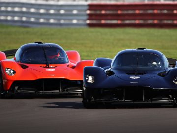 Twee krachtige Aston Martin-hypercars op een racecircuit, de ene in het blauw en de andere in het rood.