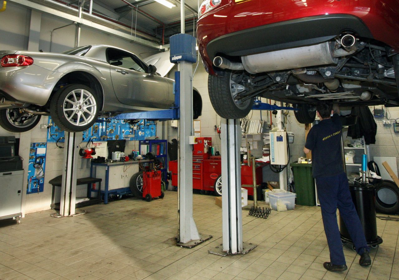 Een monteur inspecteert een auto die op een lift staat in een RDW-erkende autoreparatiewerkplaats.