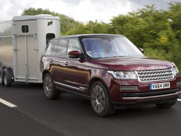 Een kastanjebruine range rover die een paardentrailer trekt en zich aan de maximale snelheid aanhanger houdt, rijdt over een snelweg.