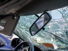 Gebroken voorruit vanuit de binnenkant van een auto met scherpgestelde achteruitkijkspiegel, voorzien van een eCall-knop.
