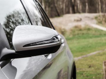 Close-up van de zijspiegel van een Mercedes-Benz GLC met een onscherpe natuurlijke achtergrond.