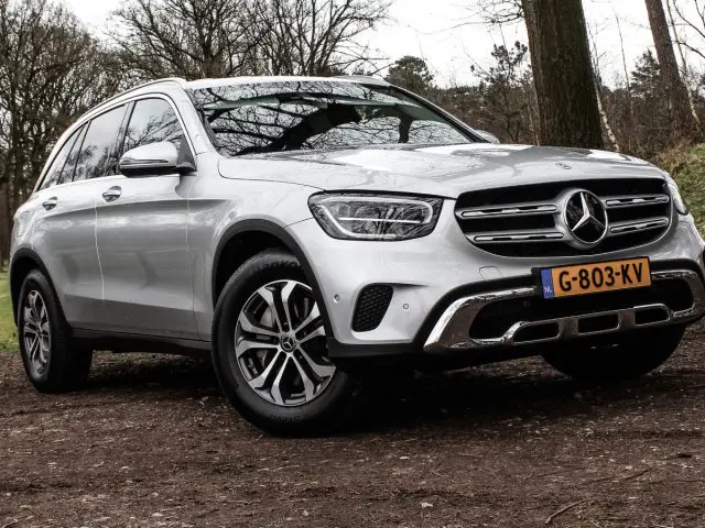 Een zilveren Mercedes-Benz GLC SUV geparkeerd op een grindpad met een bosrijke omgeving op de achtergrond.