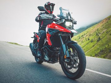 Motorrijder rijdt op een rode Suzuki-avontuurmotorfiets op een bergweg.