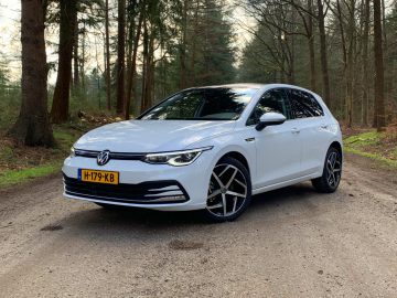 Een witte Volkswagen Golf 8 geparkeerd op een grindpad omgeven door bomen.